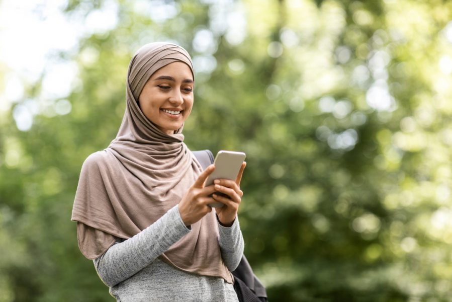 Pretty,Muslim,Woman,In,Hijab,Using,Mobile,Phone,While,Walking